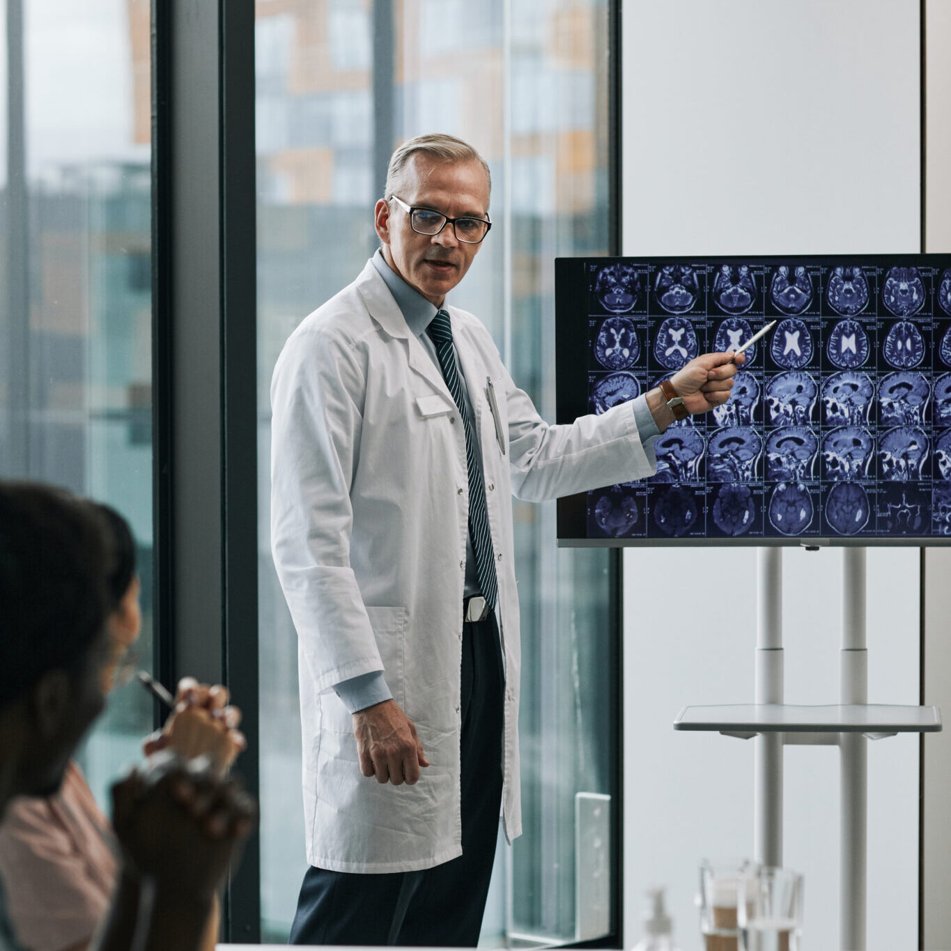 Vertical portrait of mature doctor giving presentation at medical conference and pointing at x-ray images